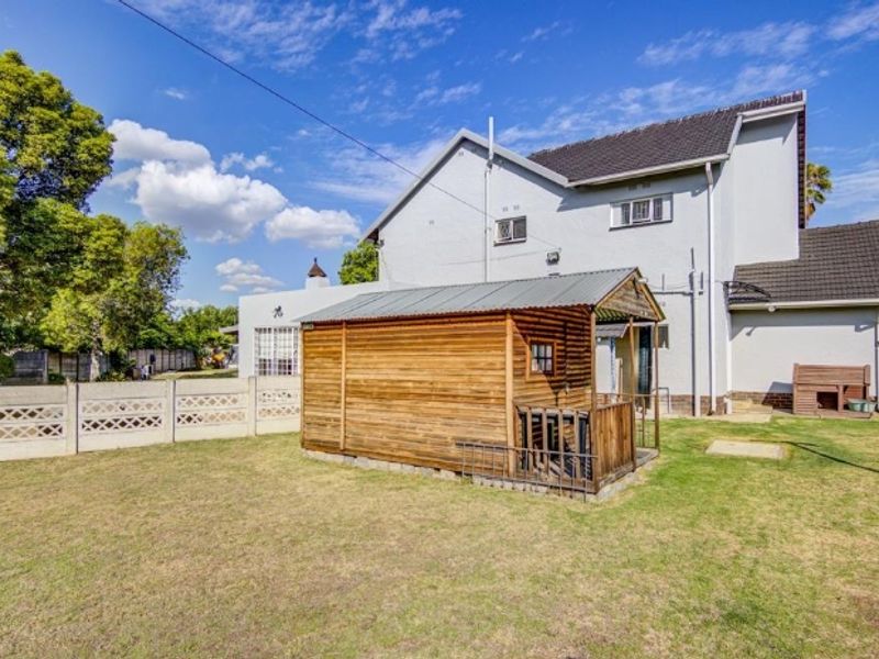 Rear view of the property featuring a lawn, precast concrete boundary wall, and a wooden garden shed structure.
