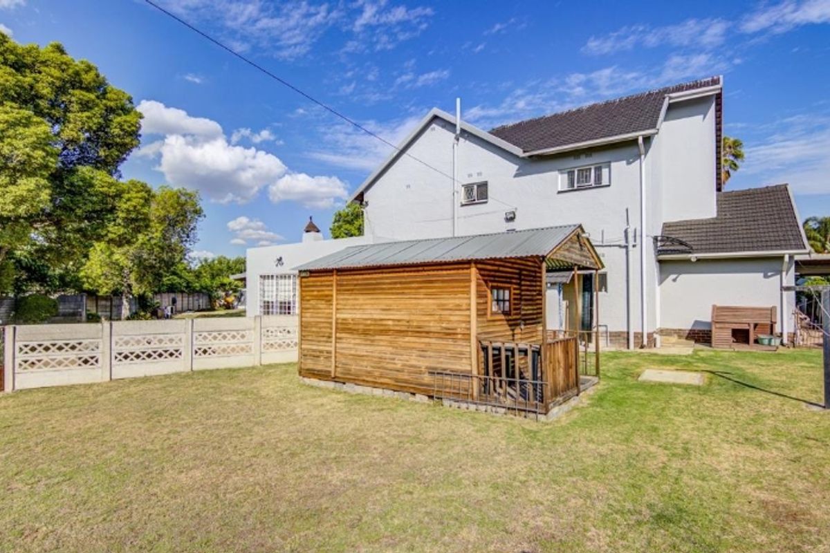 Rear view of the property featuring a lawn, precast concrete boundary wall, and a wooden garden shed structure.
