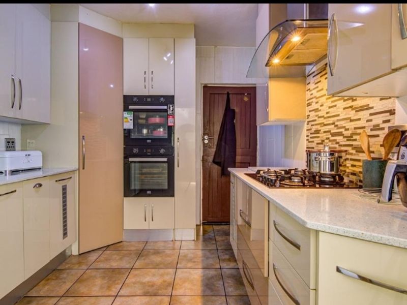 Modern kitchen featuring high-gloss cabinetry, stone countertops, a built-in double oven, gas hob, and extractor fan with tiled flooring.