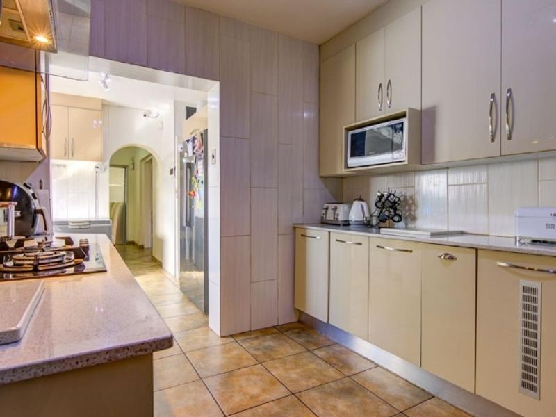 A functional kitchen featuring modern built-in cabinetry, stone countertops, a gas hob with extractor fan, and tiled flooring throughout.