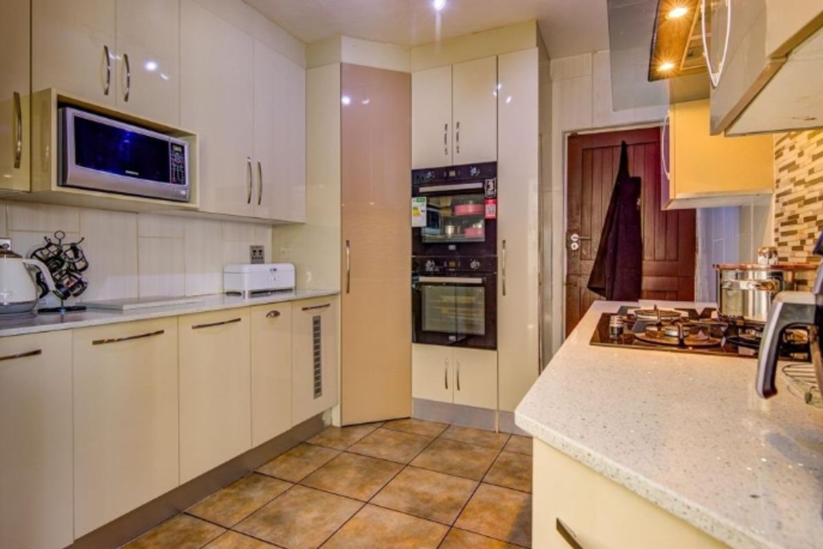 Modern kitchen featuring high-gloss cabinetry, stone countertops, built-in double oven, microwave, and gas hob with extractor fan, complemented by tiled flooring.