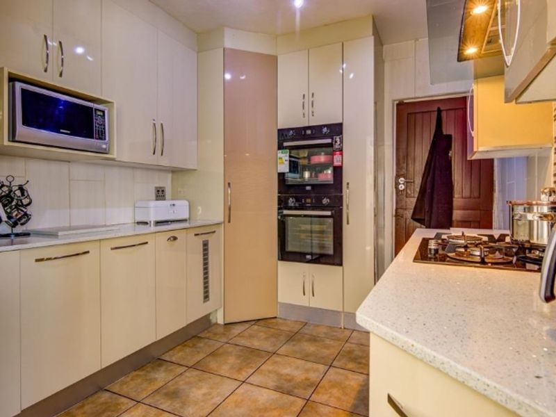 Modern kitchen featuring high-gloss cabinetry, stone countertops, built-in double oven, microwave, and gas hob with extractor fan, complemented by tiled flooring.