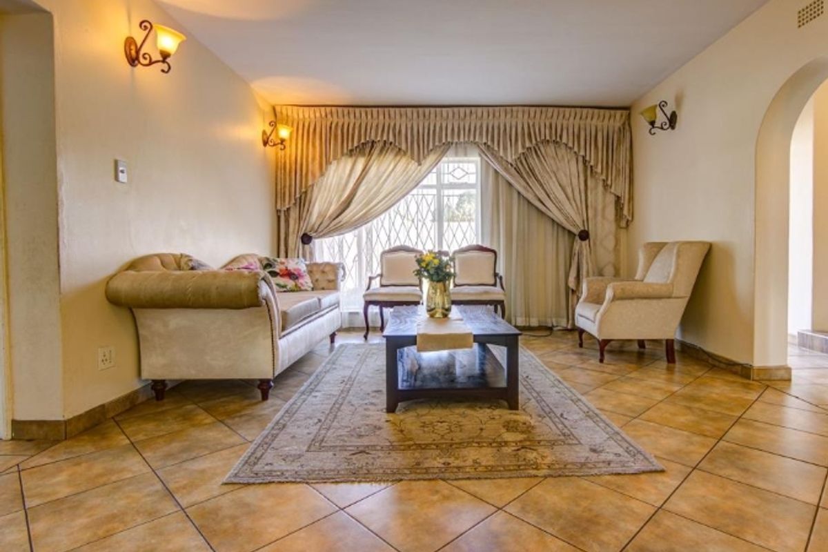A spacious living room featuring ceramic floor tiles, arched architectural details, and wall-mounted lighting, providing a comfortable and traditional living space.