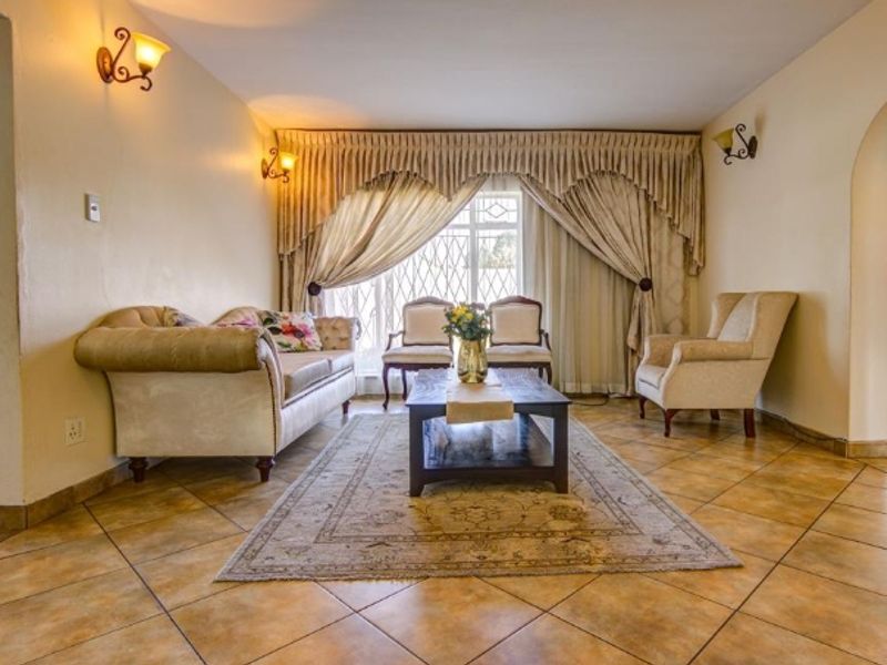 A spacious living room featuring ceramic floor tiles, arched architectural details, and wall-mounted lighting, providing a comfortable and traditional living space.