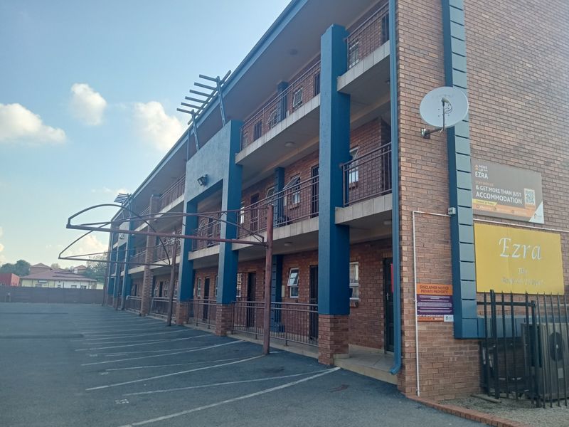 Exterior view of a multi-story face brick apartment building featuring balcony access, metal railings, and a paved parking area.