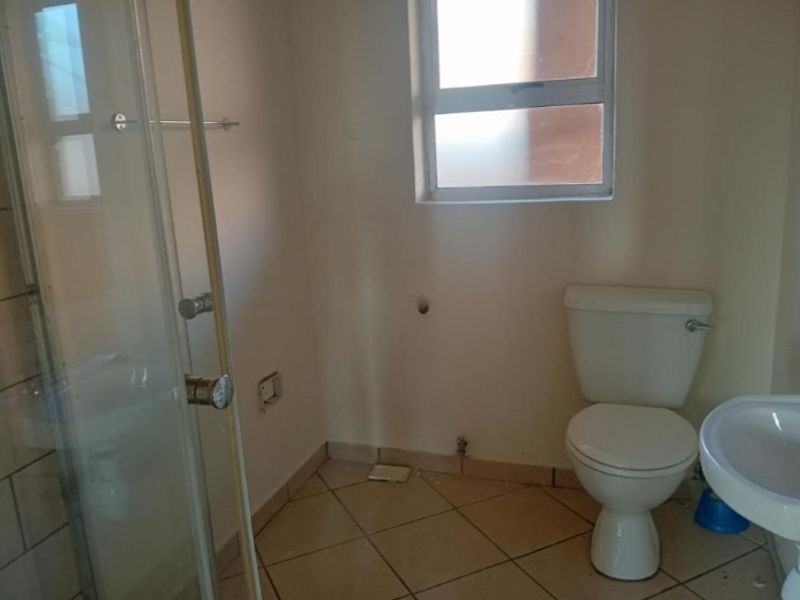 A functional bathroom featuring a shower enclosure, pedestal basin, and toilet, with tiled flooring and a window for natural light.