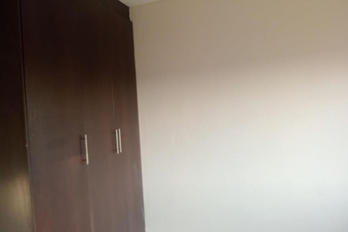 A bedroom interior featuring dark wood built-in cupboards with modern metal handles.