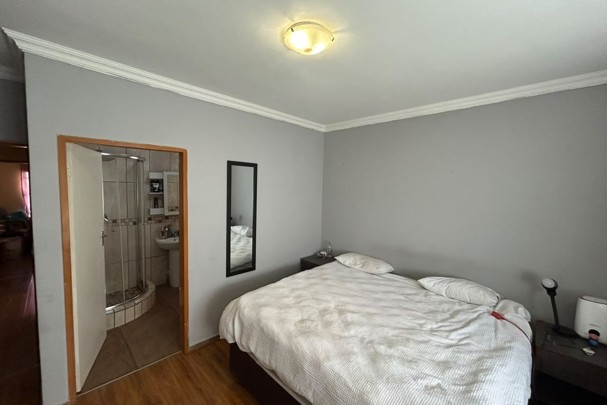 A bedroom featuring laminate flooring and an en-suite bathroom with a shower, offering a functional layout with neutral wall finishes.
