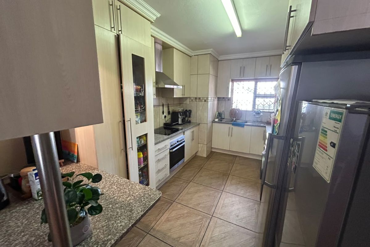 A functional kitchen featuring light-toned built-in cabinetry, granite countertops, integrated appliances, and tiled flooring with a window providing natural light.