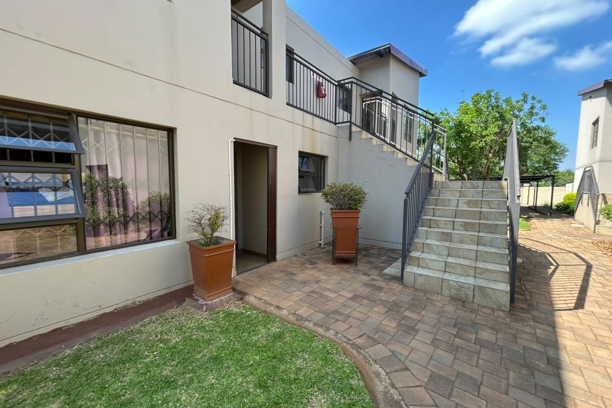 Rear exterior view featuring a paved patio area, external staircase with metal railings, and access to the building's ground floor entrance.