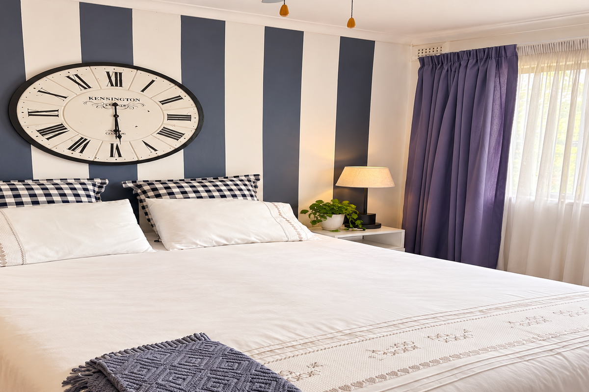 A well-maintained bedroom featuring striped accent wall, large window with layered curtains, and ceiling fan.