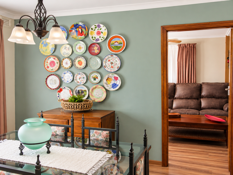 A well-maintained dining room featuring sage green accent wall, coving, and a clear transition into the adjacent living area with timber door frame.