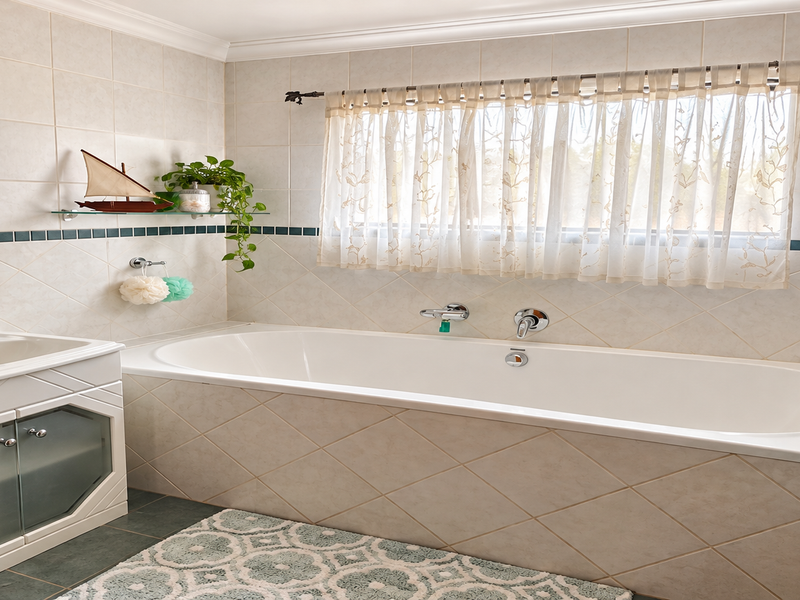 A well-maintained bathroom featuring a built-in vanity, a standard bathtub with wall-mounted fixtures, and neutral wall tiling with a decorative accent border.