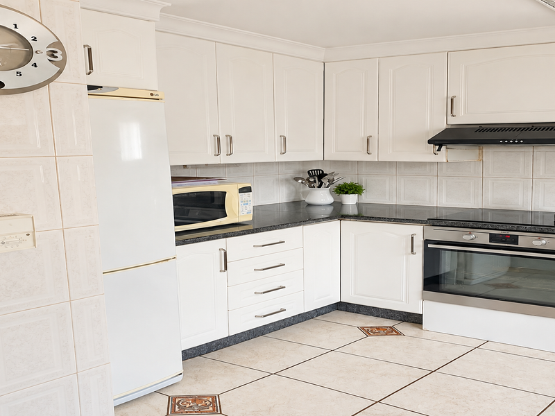 A functional kitchen featuring white cabinetry, granite countertops, tiled backsplash, and integrated appliances, with ceramic floor tiles throughout.