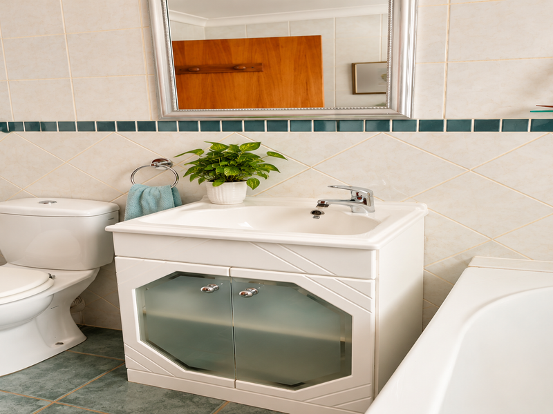A functional bathroom featuring a vanity cabinet with basin, a standard toilet, and a bathtub, finished with neutral wall tiles and green floor tiles.