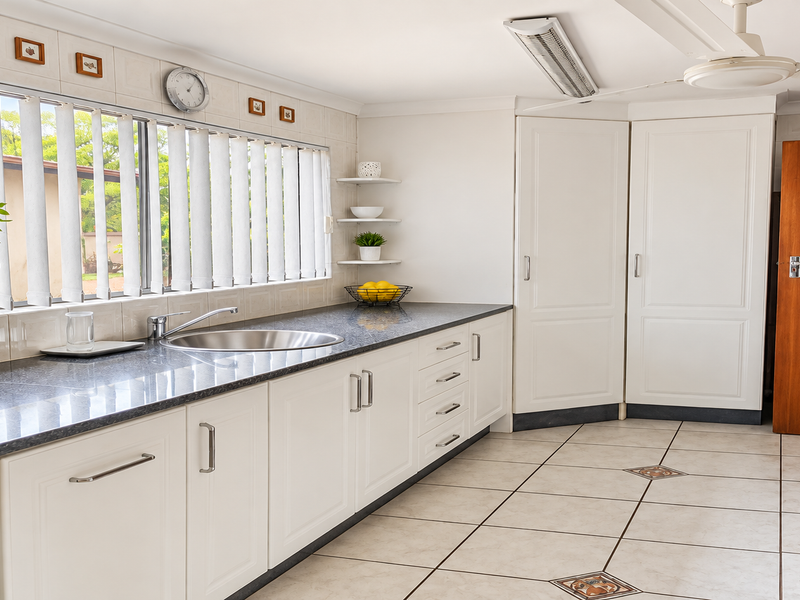 A functional kitchen featuring white cabinetry, granite countertops, a stainless steel sink, and tiled flooring with decorative accents.