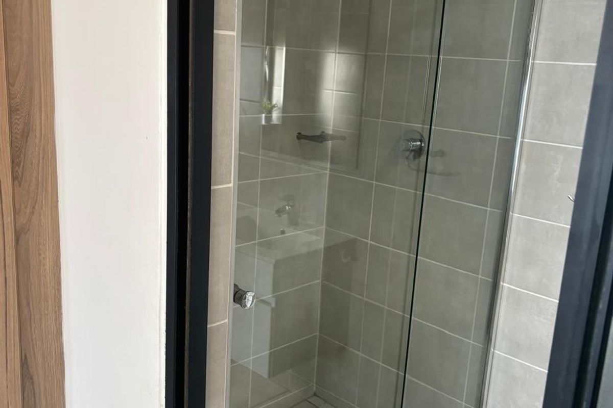 A clean, modern bathroom featuring a glass-enclosed shower with neutral wall and floor tiling.