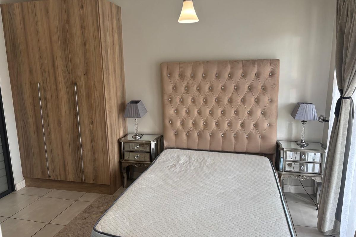 A well-maintained bedroom featuring neutral tiled flooring, a built-in wooden wardrobe, and a central pendant light fixture.