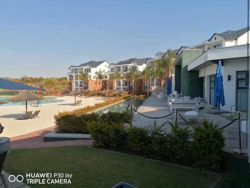 A well-maintained communal pool area featuring a swimming pool, wooden decking, and landscaped gardens within a modern apartment complex.