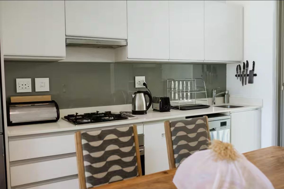 Modern kitchen featuring white cabinetry, a gas hob with extractor fan, glass splashback, and integrated dishwasher, offering a clean and functional workspace.