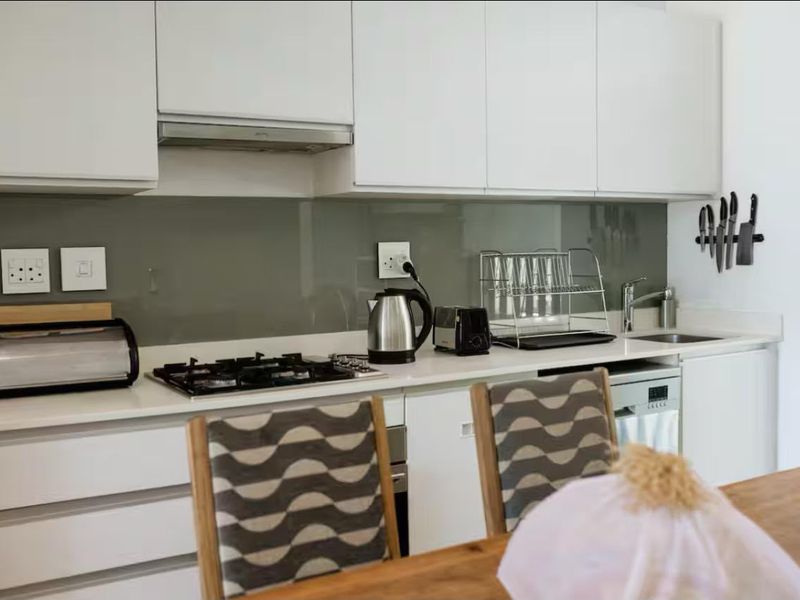 Modern kitchen featuring white cabinetry, a gas hob with extractor fan, glass splashback, and integrated dishwasher, offering a clean and functional workspace.