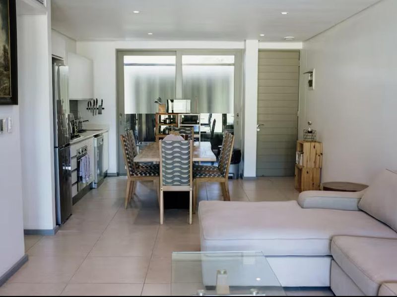 An open-plan living, dining, and kitchen area featuring tiled floors, recessed lighting, and direct access to an outdoor space through sliding glass doors.