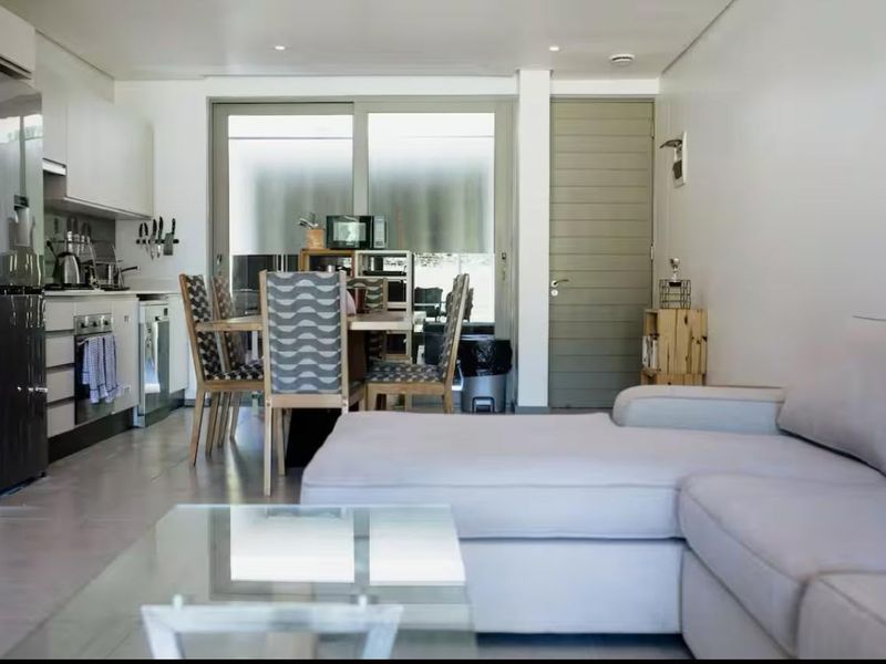 Modern open-plan living area featuring a compact kitchen with built-in cabinetry and appliances, flowing into a dining space with access to an outdoor area.