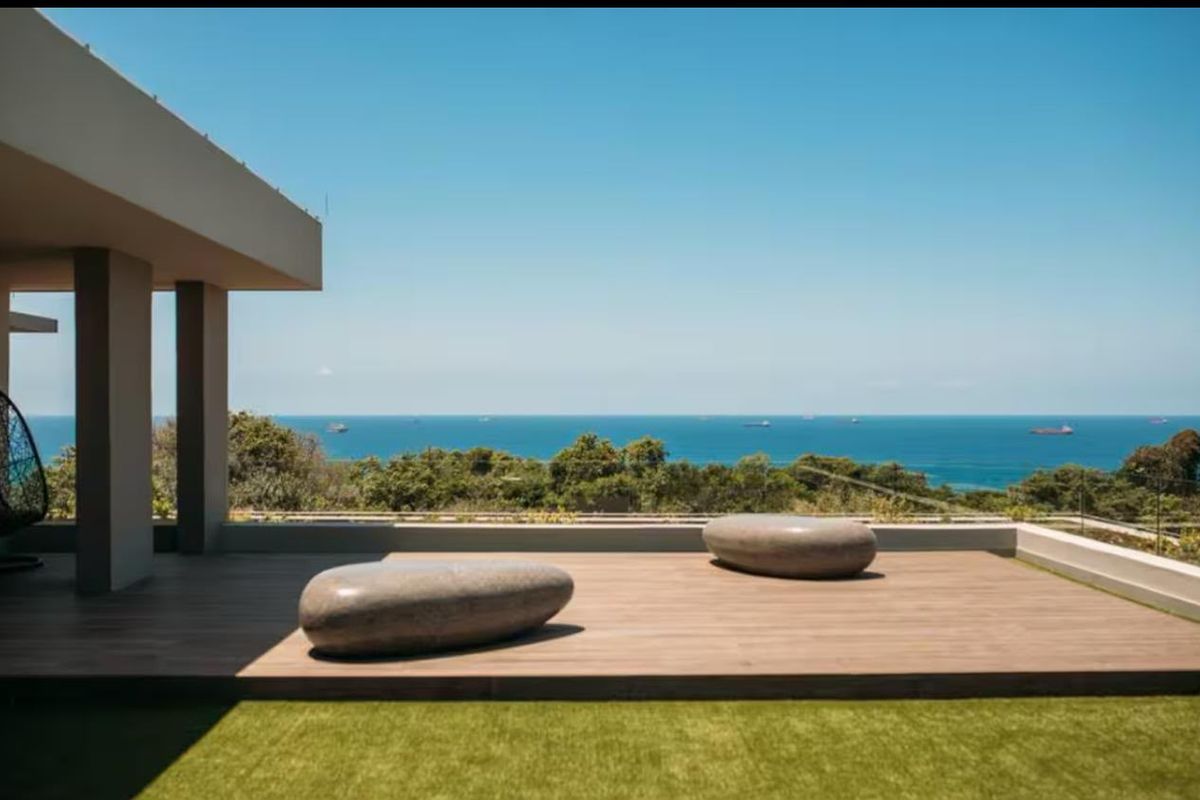 A spacious outdoor patio featuring timber decking and a glass balustrade, offering expansive, unobstructed ocean views.