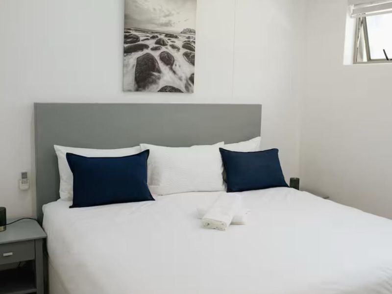 A clean and well-maintained bedroom featuring a neutral grey built-in headboard and a functional awning window for natural light.