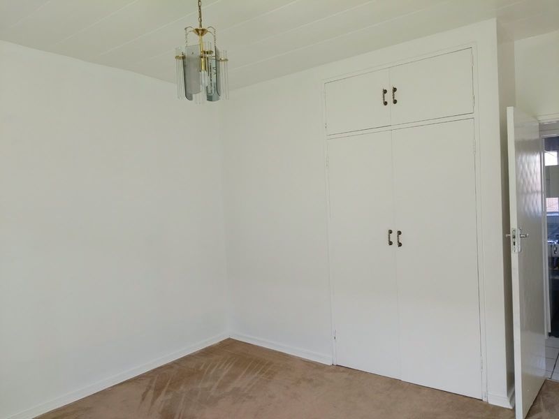 A clean, empty bedroom featuring neutral walls, built-in storage cupboards, and carpeted flooring, offering a blank canvas for personalization.