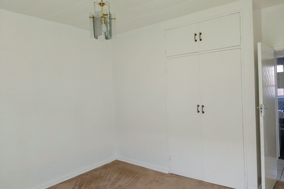 A clean, empty bedroom featuring neutral walls, built-in storage cupboards, and carpeted flooring, offering a blank canvas for personalization.