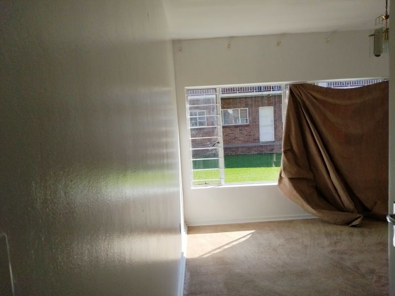 An empty living room featuring carpeted flooring and large metal-framed windows overlooking a communal garden area.