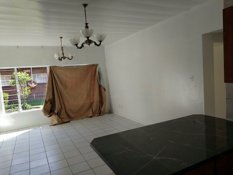 An open-plan living and dining area featuring tiled flooring, a built-in breakfast bar, and large windows providing natural light.