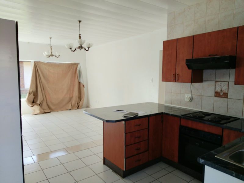 Open-plan kitchen and living area featuring tiled flooring, built-in cabinetry with laminate countertops, and integrated cooking appliances.