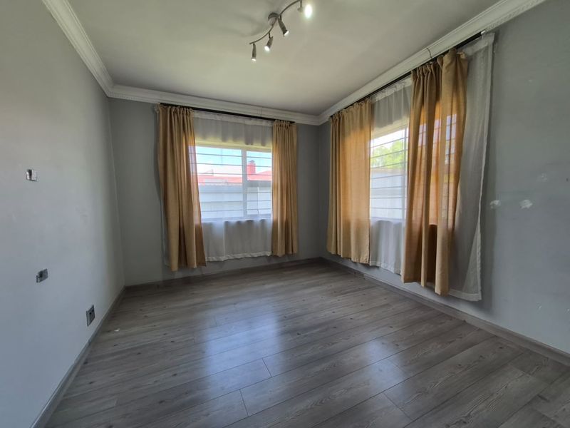 A bright, empty bedroom featuring modern laminate flooring, ceiling cornicing, and security bars on the windows, ready for personalization.