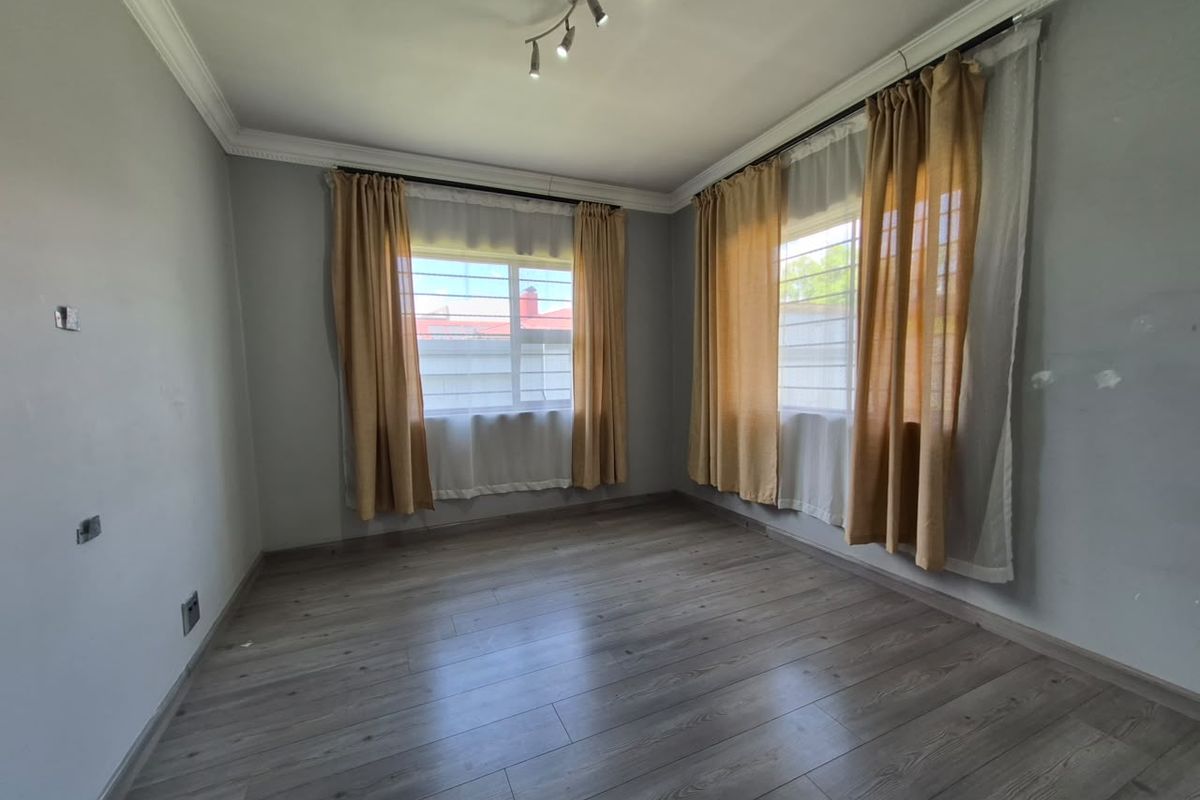 A bright, empty bedroom featuring modern laminate flooring, ceiling cornicing, and security bars on the windows, ready for personalization.