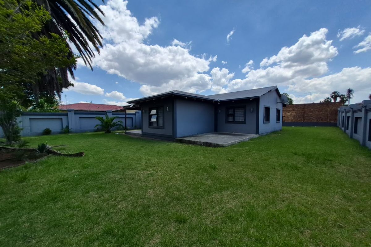 Rear view of the house featuring a concrete patio, expansive lawn, and secure perimeter walling.