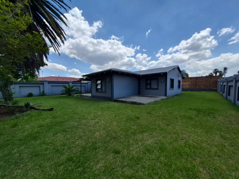 Rear view of the house featuring a concrete patio, expansive lawn, and secure perimeter walling.