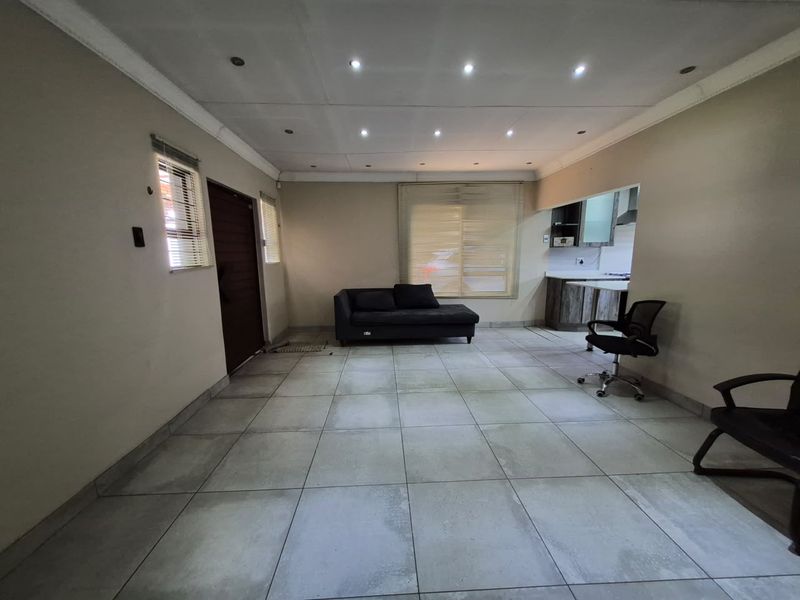 Open-plan living area featuring large format floor tiles, recessed ceiling lights, and a partial view into the adjacent kitchen space.