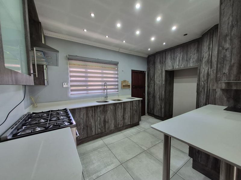Modern kitchen featuring dark wood-grain cabinetry, stone countertops, a gas hob with extractor, and tiled flooring with recessed ceiling lighting.