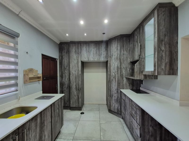 Modern kitchen featuring dark wood-grain cabinetry, white stone countertops, integrated hob, and tiled flooring with recessed lighting.