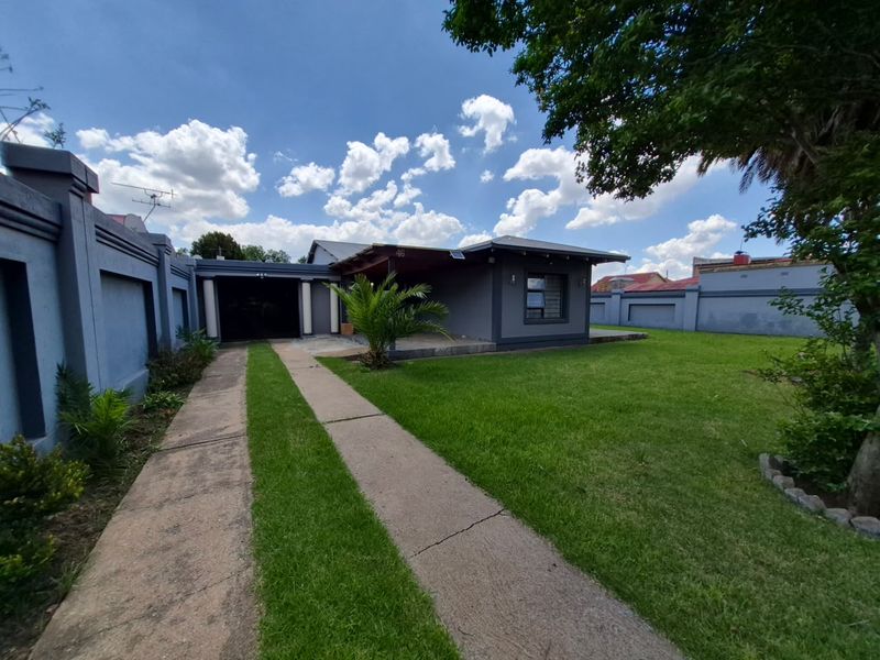 Front view of a single-story house featuring a concrete driveway, perimeter wall, and a covered entrance area set within a landscaped garden.