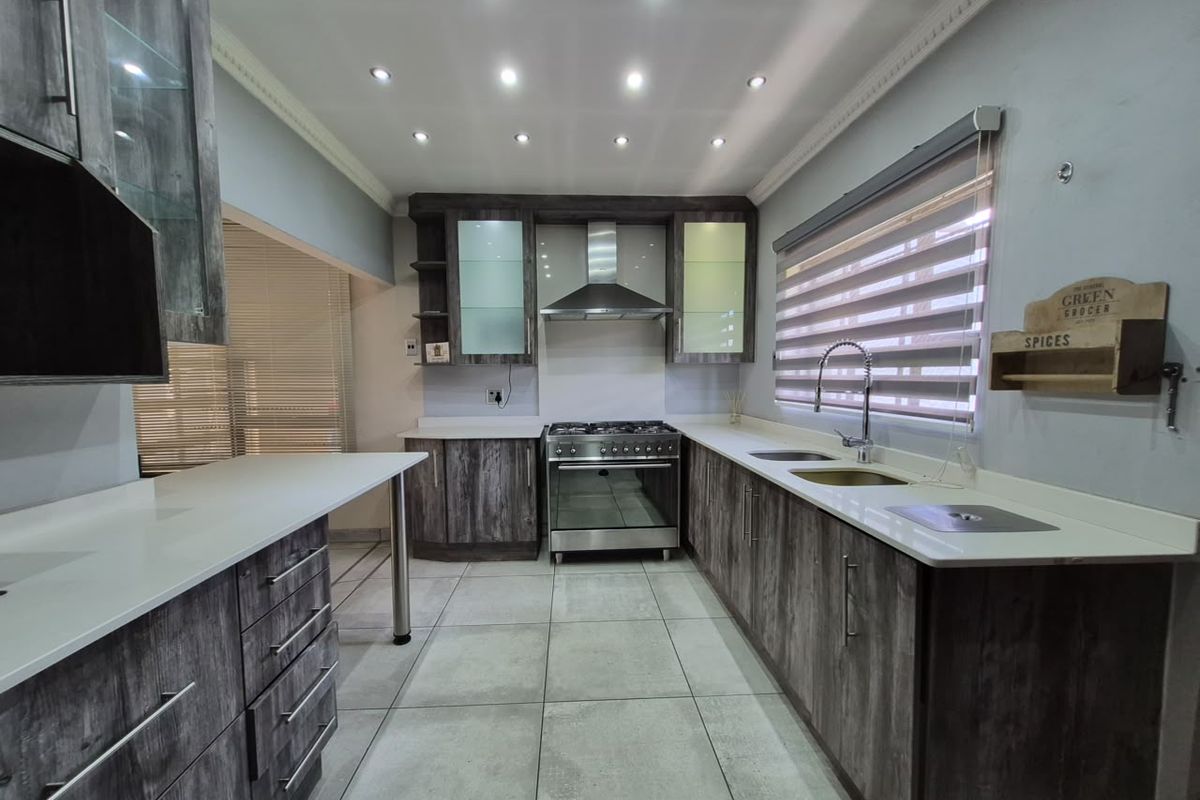 Modern kitchen featuring wood-grain cabinetry, stone countertops, stainless steel gas stove, extractor fan, and recessed lighting with tiled flooring.