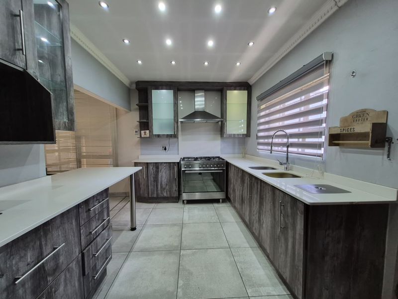 Modern kitchen featuring wood-grain cabinetry, stone countertops, stainless steel gas stove, extractor fan, and recessed lighting with tiled flooring.