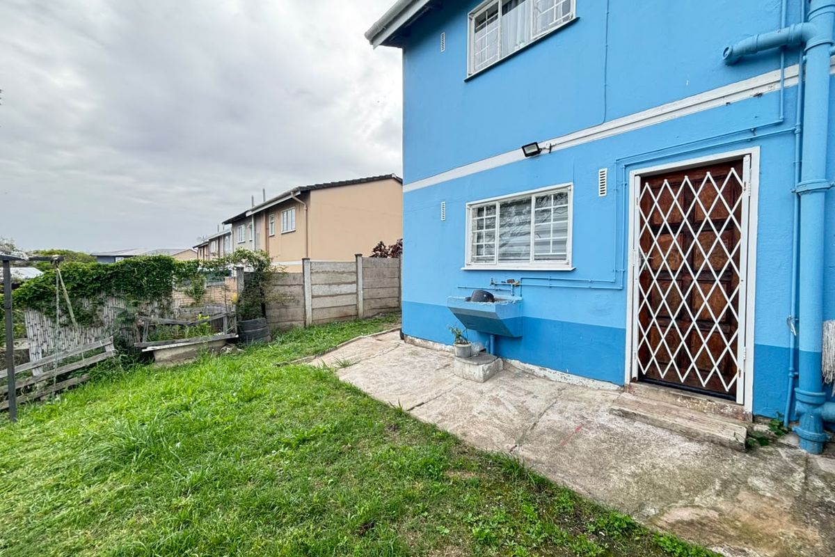 Rear exterior view of the property featuring a concrete patio, security gate, and an external wash basin against a blue painted wall.