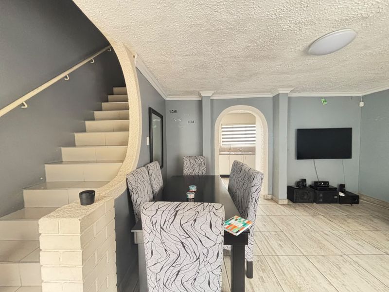 Open plan living and dining area featuring a prominent staircase, tiled flooring, and an arched entryway leading to the kitchen.