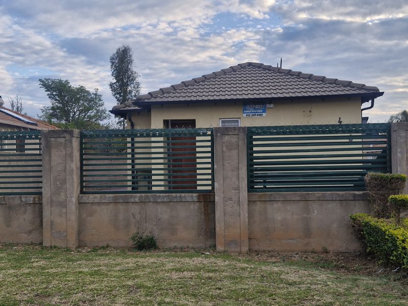 Front view of a residential property featuring a concrete boundary wall with metal fencing, a tiled roof, and an integrated solar water heating system.