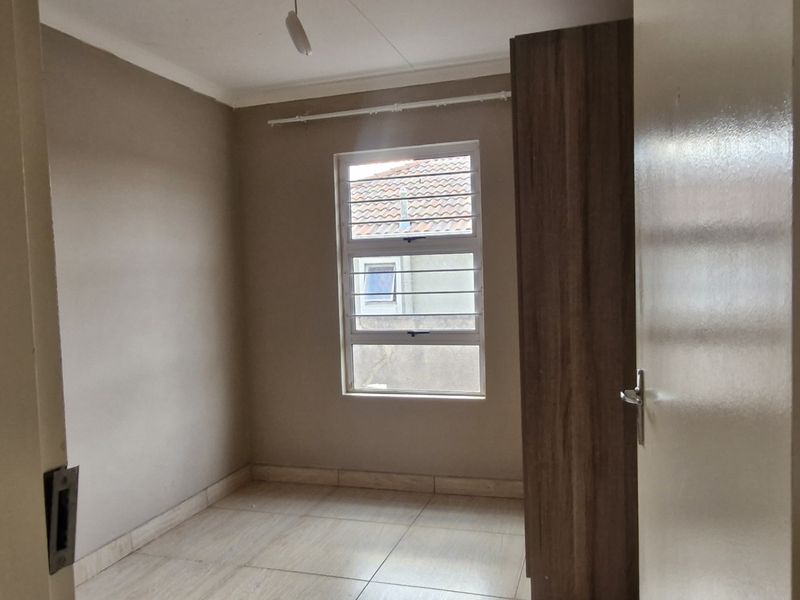 A clean, empty bedroom featuring tiled flooring, a built-in cupboard, and a window with security bars.