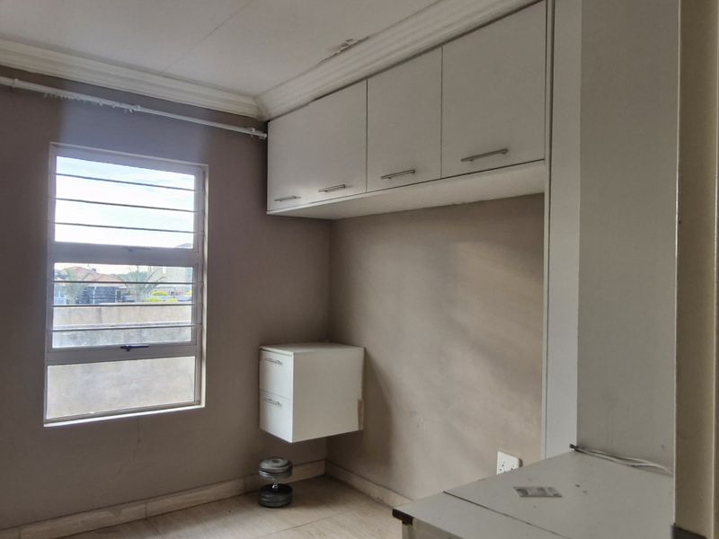 A compact bedroom featuring built-in overhead storage, wall-mounted cabinetry, tiled flooring, and a window with security bars, offering a functional space for renovation.