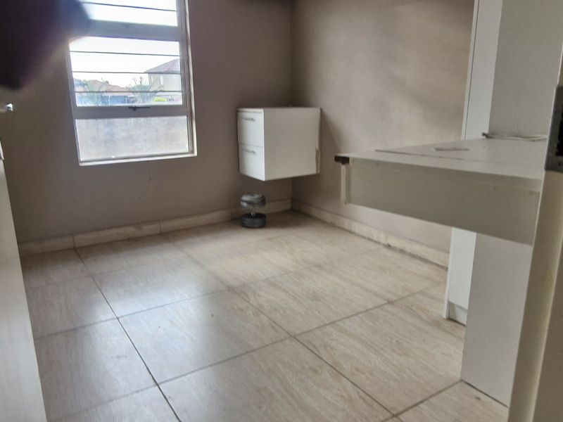 A compact bedroom featuring tiled flooring, a built-in desk, and a wall-mounted cabinet, offering a functional space ready for personalization.